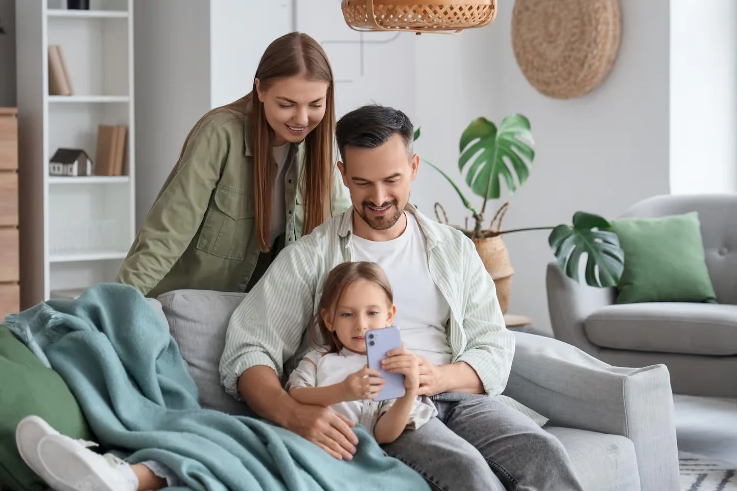 Parents and their young daughter smiling together on a living room sofa